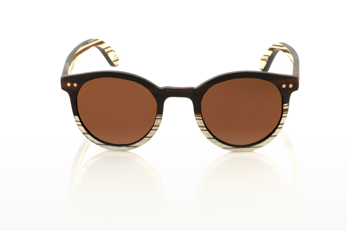 Gafas de Madera Natural de Ébano ATHENEA. Gafas de sol de madera ATHENEA, con su diseño compacto y redondeado y una ceja pronunciada similar a los modelos LANA y LINDA, se destacan por su elegancia y originalidad. Fabricadas con una combinación única de madera de ébano en la parte superior del frontal y zebra blanca en la inferior, estas gafas ofrecen un contraste visual impresionante que capta la atención. Además, el frontal se enriquece con dos incrustaciones redondas de madera de haya, añadiendo un detalle distintivo y un toque de sofisticación. Con una medida de 135x47mm y un calibre de 45, las ATHENEA son ideales para quienes buscan gafas más pequeñas sin sacrificar el estilo ni la presencia.  Venta al Por Mayor y Detalle | Root Sunglasses® 